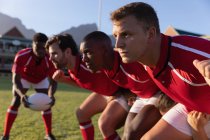 Vista lateral de jogadores de rugby multi étnicos masculinos que se preparam para um scrum no estádio em um dia ensolarado — Fotografia de Stock