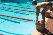 Seitenansicht eines jungen männlichen kaukasischen Schwimmers, der an sonnigen Tagen konzentriert auf dem Startblock in Startposition im Freibad steht — Stockfoto