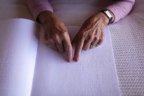 Close-up de uma mulher cega ativa sênior lendo um livro de braille com os dedos na cama no quarto em casa — Fotografia de Stock
