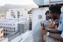 Vista lateral de Macho multi amigos étnicos interagindo uns com os outros, tendo cerveja nas mãos na varanda — Fotografia de Stock