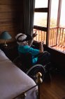 Вид збоку на активну старшу жінку з використанням гарнітури віртуальної реальності, сидячи на інвалідному візку в спальні вдома — стокове фото
