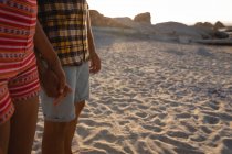 Средняя часть афро-американской пары стоит на пляже на песке. Держась за руки друг друга на закате — стоковое фото