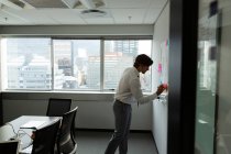 Side view of handsome young male executive writing on sticky notes in a modern office — Stock Photo