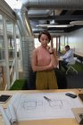 Vista frontal de uma empresária asiática pensativa em pé no escritório e olhando para o modelo na mesa — Fotografia de Stock