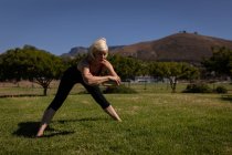 Vista frontale di una donna anziana attiva che si allena e si allunga nel parco in una giornata di sole — Foto stock