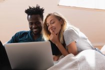 Фронтальний вид multi етнічних пара посміхаючись, сидячи і використання ноутбука вдома на дивані — стокове фото