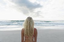 Rear view of beautiful woman standing at beach on a sunny day. She is watching the ocean — Stock Photo