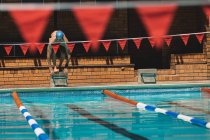 Vista frontal de un joven nadador caucásico listo para saltar al agua de una piscina al aire libre en un día soleado - foto de stock
