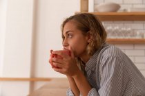 Vista lateral da mulher pensativa tendo xícara de chá enquanto está em pé na sala de cozinha — Fotografia de Stock
