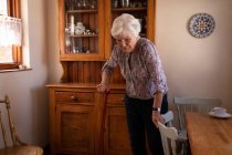 Vorderansicht einer aktiven Seniorin, die zu Hause mit einem Stock in der Küche spaziert — Stockfoto