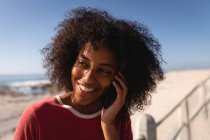 Nahaufnahme einer afrikanisch-amerikanischen Frau, die am Strand lächelt und mit ihrem Handy telefoniert — Stockfoto