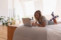 Красива жінка використовує ноутбук вдома, лежачи на ліжку вдома — стокове фото
