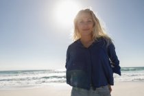 Retrato de mulher loira bonita de pé na praia em um dia ensolarado. Ela está olhando e sorrindo para a câmera — Fotografia de Stock