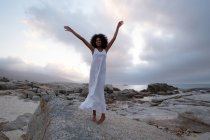 Low section of African-american woman standing with opened arm near sea side in dusk — Stock Photo