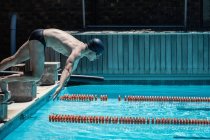 Vue latérale du jeune nageur masculin caucasien sautant dans l'eau d'une piscine extérieure le jour ensoleillé — Photo de stock
