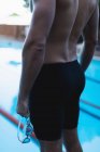 Середина чоловічого плавця, що стоїть перед басейном з плаваючими окулярами в руці — стокове фото