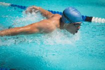 Close-up of young Caucasian male swimmer swimming butterfly stroke in outdoor swimming pool on sunny day — Stock Photo