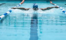 Vue de face du jeune nageur masculin caucasien nageant coup de papillon dans la piscine extérieure au soleil — Photo de stock