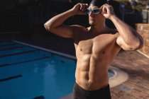 Vorderansicht eines männlichen kaukasischen Schwimmers, der seine Schwimmbrille trägt, während er an einem sonnigen Tag in der Nähe eines Schwimmbades steht — Stockfoto