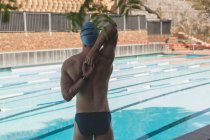 Rückansicht einer jungen kaukasischen Schwimmerin mit Badekappe und Badebekleidung, die sich vor dem Freibad dehnt — Stockfoto