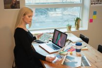 Вид збоку вдумлива кавказька бізнес-леді дивиться через ноутбук і тримає планшет в руці в офісі — стокове фото