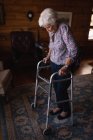 Vista lateral de una mujer mayor activa caminando con un andador en la sala de estar en casa - foto de stock
