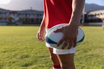 Seção intermediária de um jogador de rugby masculino segurando a bola de rugby e de pé no estádio — Fotografia de Stock