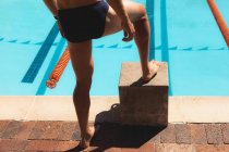 Baixa seção de nadador masculino de pé com um pé no bloco de entradas na piscina exterior no dia ensolarado — Fotografia de Stock