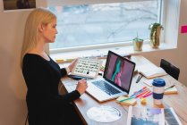 Vista lateral da empresária caucasiana pensativa olhando sobre o laptop e segurando tablet no escritório — Fotografia de Stock