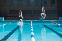 Vista frontale di nuotatori caucasici maschi e femmine che saltano in acqua nello stesso momento alla piscina sotto il sole — Foto stock