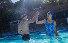 Vista lateral de jovens nadadores do sexo masculino e feminino dando alta cinco uns aos outros na piscina — Fotografia de Stock