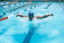 Vista frontal do jovem nadador caucasiano nadador nadar acidente vascular cerebral borboleta na piscina ao sol — Fotografia de Stock