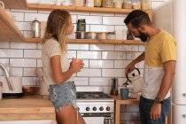 Side view of multi race couple talking with each other at home in kitchen room — Stock Photo