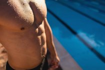 Seção intermediária de um nadador masculino em pé perto da piscina em um dia ensolarado — Fotografia de Stock
