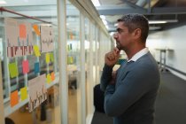 Side view of a thoughtful businessman looking over sticky notes fixed on the wall in office — Stock Photo