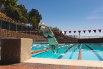 Vista de ángulo bajo de un joven nadador caucásico buceando en el agua de una piscina al aire libre en un día soleado - foto de stock
