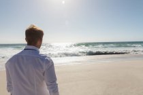 Вид сзади на расслабленного мужчину, стоящего на пляже в солнечный день. Он идет. — стоковое фото