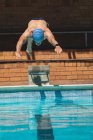 Vue de face du jeune nageur masculin caucasien plongeant dans l'eau d'une piscine extérieure le jour ensoleillé — Photo de stock
