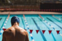 Задній вид молодих кавказьких чоловіків плавець дивлячись, поки стоїть біля плавального басейну на сонці — стокове фото