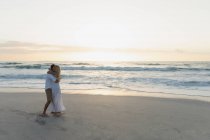 Вид збоку молодої пари кохання обіймає один одного, стоячи на пляжі. Вони насолоджуються відпусткою — стокове фото