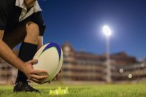 Low angle view of a rugby player placing the rugby ball on the kicking tee in the stadium at night — Stock Photo