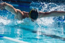 Vista frontal de un nadador masculino nadando mariposa estilo libre en la piscina en un día soleado - foto de stock