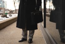 Niedriger Abschnitt gut gekleideter Geschäftsmann, der an einem verschneiten Tag in der Stadt auf dem Bürgersteig steht — Stockfoto