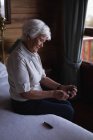 Vista lateral de uma mulher idosa ativa verificando seu nível de açúcar no sangue com um glicosímetro na cama no quarto em casa — Fotografia de Stock