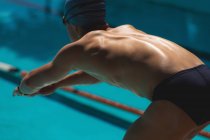 Close-up of young Caucasian male swimmer in starting position at swimming pool on sunny day — Stock Photo
