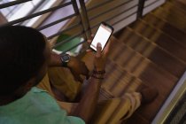 Vue en grand angle d'un homme d'affaires afro-américain utilisant un téléphone portable à l'escalier dans son bureau — Photo de stock
