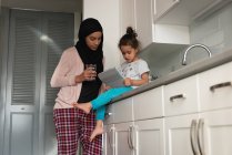 Vista a basso angolo della madre di razza mista che indossa hijab e figlia insieme utilizzando tablet digitale nella stanza della cucina a casa — Foto stock