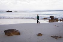 Vista laterale di una donna anziana attiva che cammina sul lungomare della spiaggia — Foto stock