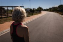 Rückansicht einer aktiven Seniorin, die in der Sonne steht und auf die Straße blickt — Stockfoto