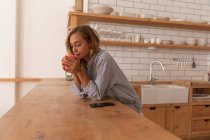 Vista lateral da mulher tomando uma xícara de chá enquanto está na sala da cozinha em casa — Fotografia de Stock
